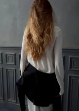 Blusa de manga larga en color crema, con cuello alto y diseño de drapeado suave en la parte frontal. Presenta un corte recto y elegante.
