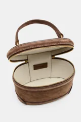 Bolso formato vanity de gamuza color marrón, con asa de mano superior y correa bandolera extraíble y ajustable. Presenta cierre de doble cremallera metálica dorada y detalles de pespuntes en el cuerpo.
