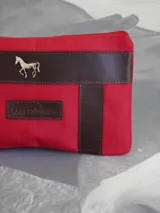 Sobre cartuchera de lona naranja con detalles en cuero marrón, cierre superior y aplique metálico de caballo en el frente.