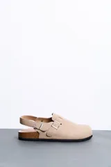 Sandalias estilo zueco color beige con tira trasera ajustable, hebillas metálicas plateadas, suela de corcho y base de goma negra.