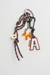 Llavero decorativo con cordón de nylon marrón con detalles reflectantes, que incluye una letra 'D' de plástico, un dije de perro tipo globo de resina naranja y un dije de letra 'A' de goma con borde marrón. Cuenta con una argolla metálica y un mosquetón negro.