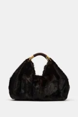 Maxi bolso de mano con acabado de pelo sintético en color marrón oscuro. Presenta un diseño estructurado con doble asa de mano reforzada y detalles metálicos dorados en las uniones. Cuenta con cierre mediante botón imantado y forro interior con bolsillo con cremallera.