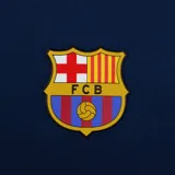 Camiseta de fútbol del FC Barcelona, color azul marino con mangas de distinto color (rojo y azul), escudo del club en el pecho y logo de la marca deportiva.