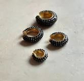 Set de tres aros trepadores con brillos, uno en tono bronce con piedras negras, uno dorado con piedras transparentes y uno plateado con piedras transparentes.