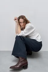 Jean wide leg negro de tiro alto, confeccionado en denim rígido, con diseño de cinco bolsillos, presillas para cinto, cierre frontal con botón y ruedo desflecado.