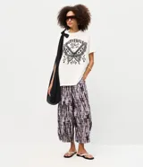 Pantalón aladín de cintura alta confeccionado en viscosa texturizada con estampado tie-dye en tonos oscuros. Presenta un corte amplio con volumen en las piernas y bajos afinados.