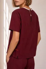 Blusa de lino color beige, de manga corta y cuello redondo, con detalles de costuras decorativas verticales y una línea horizontal bordada en tono contrastante.
