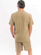 Camisa de manga corta color beige, con cuello mao, bolsillo ojal en el pecho y cierre frontal parcial con botones.