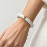 Pulsera rígida de metal esmaltado blanco con aplique dorado central decorado con pequeñas circonias incrustadas.
