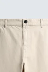 Pantalón chino de algodón color beige claro, corte recto, con cierre frontal de cremallera y botón, bolsillos delanteros y bolsillos traseros de doble vivo con botón.