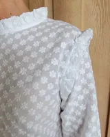 Blusa blanca de manga larga con cuello alto y volados en cuello y hombros.