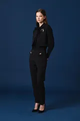 Pantalon de vestir color verde oscuro, de corte recto y tiro alto. Presenta dos solapas decorativas en la cintura con apliques de broches metálicos con forma de insectos.