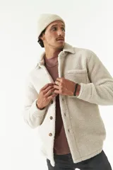 Sobrecamisa de sherpa color crema con cuello camisero, cierre frontal con botones a presión y bolsillo de parche en el pecho. El modelo usa talle M.