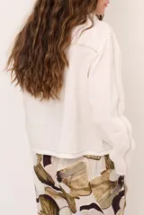 Chaqueta de lino color beige, de manga larga, con cuello redondo y cierre frontal de botones a presión con solapa.
