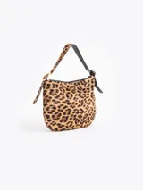 Cartera tipo hobo confeccionada en cuero con pelo vacuno estampado animal print. Presenta correa de hombro ajustable con detalles de hebillas metálicas en los laterales y cierre superior.