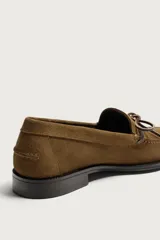 Mocasín de vestir para hombre confeccionado en piel con acabado en gamuza de color marrón, con punta redonda, suela oscura con ligero tacón y detalle de lazo en el empeine.