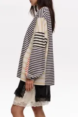 Remera manga larga oversize de corte relajado, confeccionada en 100% algodón orgánico con cuello redondo. Presenta un diseño de rayas horizontales en combinación de tonos azul marino, beige, blanco y detalles en rojo.