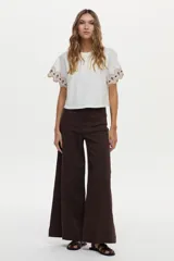 Blusa blanca de jersey con mangas cortas amplias de tela plana, decoradas con bordados geométricos en tonos marrón y azul marino.