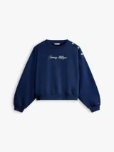 Buzo de felpa Tommy Hilfiger color azul marino, de corte regular y manga larga, con cuello redondo y puños y bajo en punto canalé. Presenta detalle de botones dorados decorativos en el hombro y logotipo de la marca bordado en tipografía script en el pecho.