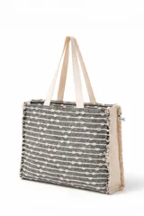 Bolso tote bag tejido a mano, color gris oscuro con rayas horizontales y puntos en relieve color crema. Tiene asas de tela color crema y bordes deshilachados.