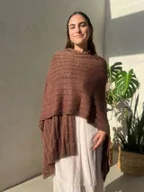 Ruana tejida en punto jersey, color negro con destellos brillantes de lurex. Presenta una etiqueta de cuero sintético con logo en la parte posterior.