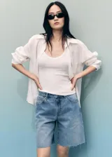 Short de jean estilo bermuda con tiro medio, diseño recto y cinco bolsillos. Presenta cierre frontal con cremallera y botón, con detalle de bajo deshilachado.