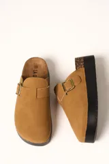 Zueco de plataforma color camel, confeccionado en material tipo gamuza, con detalle de hebilla metálica lateral y base de corcho con suela de goma negra.