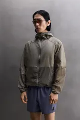 Chaqueta cortavientos de tejido técnico con estructura ripstop, cuello subido con capucha, cierre frontal de cremallera, bolsillos laterales ocultos y zonas perforadas para mayor transpirabilidad.