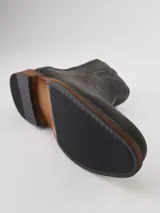 Bota Chelsea de gamuza gris con elásticos laterales, suela de goma marrón y tirador trasero.