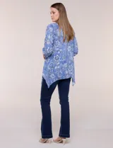 Blusa azul con estampado floral, escote en V, abotonadura frontal y mangas tres cuartos con presilla para arremangar. Cuenta con un diseño amplio y ruedo asimétrico en punta.