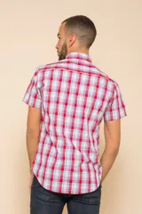 Camisa de manga corta con estampado de cuadros en tonos verdes, azules y blancos. Presenta cuello clásico, cierre frontal con botones y dos bolsillos delanteros con solapa.