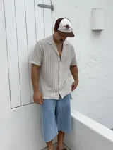 Camisa tejida a rayas verticales color beige y blanco, de corte recto, manga corta y cuello cubano.