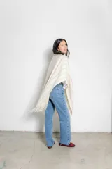 Ruana color crudo con diseño tejido a rayas verticales en tonos beige y flecos en el borde inferior.