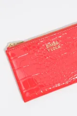 Monedero de estructura rígida con acabado brillante y textura efecto cocodrilo, cierre de cremallera superior con tirador de tela y logo metálico frontal.