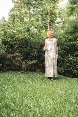 Vestido largo de corte recto y holgado, con cuello tipo polera drapeado y sin mangas. Presenta un estampado abstracto en tonos grisáceos y beige.