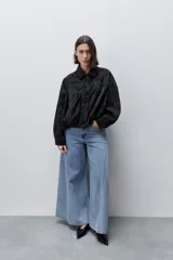 Campera marrón de poliuretano con acabado texturizado, silueta relajada, cuello camisero, cierre frontal, hombros caídos y mangas amplias con efecto abombado.