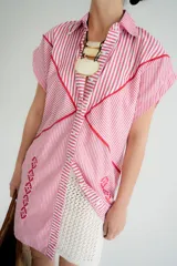 Vestido camisero a rayas verticales rojas y blancas con bordados florales rojos. Tiene cuello camisero, cierre frontal con botones y mangas cortas.