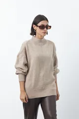Polera de tejido de punto color gris, con cuello alto, mangas largas abullonadas con puños elásticos y costura central vertical en el frente. Presenta una abertura sutil en la espalda.