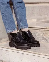 Botinetas de caña baja con suela track gruesa, combinando cuero negro en la puntera, gamuza marrón en el lateral y detalles de textura animal print tipo serpiente en tonos marrones. Presenta un cierre de solapa con velcro en el empeine.