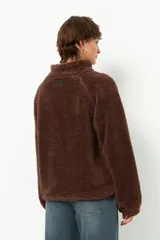 Buzo negro de teddy con cuello alto y cierre de cremallera parcial. Presenta bolsillos de nylon en la parte inferior delantera.