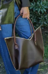 Cartera de cuero mediana con manijas largas, diseño con borde superior en corte en V y terminación artesanal con costuras contrastantes.