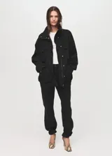 Anorak de estilo utilitario confeccionado en tejido de algodón tipo denim, con diseño oversize, cuello embudo, cierre frontal de cremallera y botones a presión, y cuatro bolsillos de parche con solapa en la parte delantera.