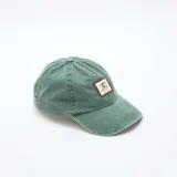 Gorra de tela verde con efecto desgastado, visera curva y parche rectangular frontal de cuerina marrón con diseño bordado de montaña y texto "Wild Life".
