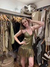 Vestido corto dorado con escote en V, cut outs laterales bajo el busto, breteles finos que se cruzan en la espalda y atan atrás, busto, pieza bajo busto y cinto cadera en tela combinada y dos volados en el ruedo.