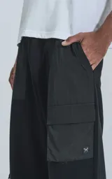 Pantalón tipo jogger negro, de calce relajado, confeccionado en algodón y microfibra. Presenta paneles de microfibra en la parte superior y bolsillos cargo con fuelle en las piernas. Los tobillos son ajustables con cordón elástico.