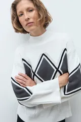 Media polera de tejido de punto color crudo, con diseño de rombos en el frente en tonos gris y negro. Presenta cuello alto y mangas largas.