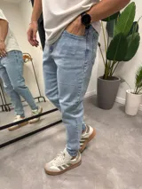 Jean de corte skinny en color azul claro, confeccionado en denim con elastano. Presenta un diseño clásico de cinco bolsillos y cierre frontal con botón y cremallera.