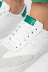 Zapatillas acordonadas de cuero color blanco con puntera de gamuza gris y detalles en verde.