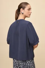 Blusa de manga corta color negro, con calce relajado, escote redondo con abertura y lazo para anudar. Presenta detalles de tablas horizontales en la parte superior que aportan textura al diseño.