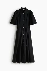 Vestido largo negro de popelina de algodón con alforzas, inserciones de encaje, manga corta abullonada, cuello camisero, botonadura frontal y cinturón fino para atar en la cintura.